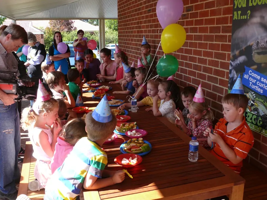 Children in party hats along a long table at the zoo
